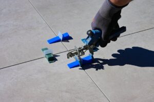 A gloved hand using a leveling tool to install tiles with spacers.