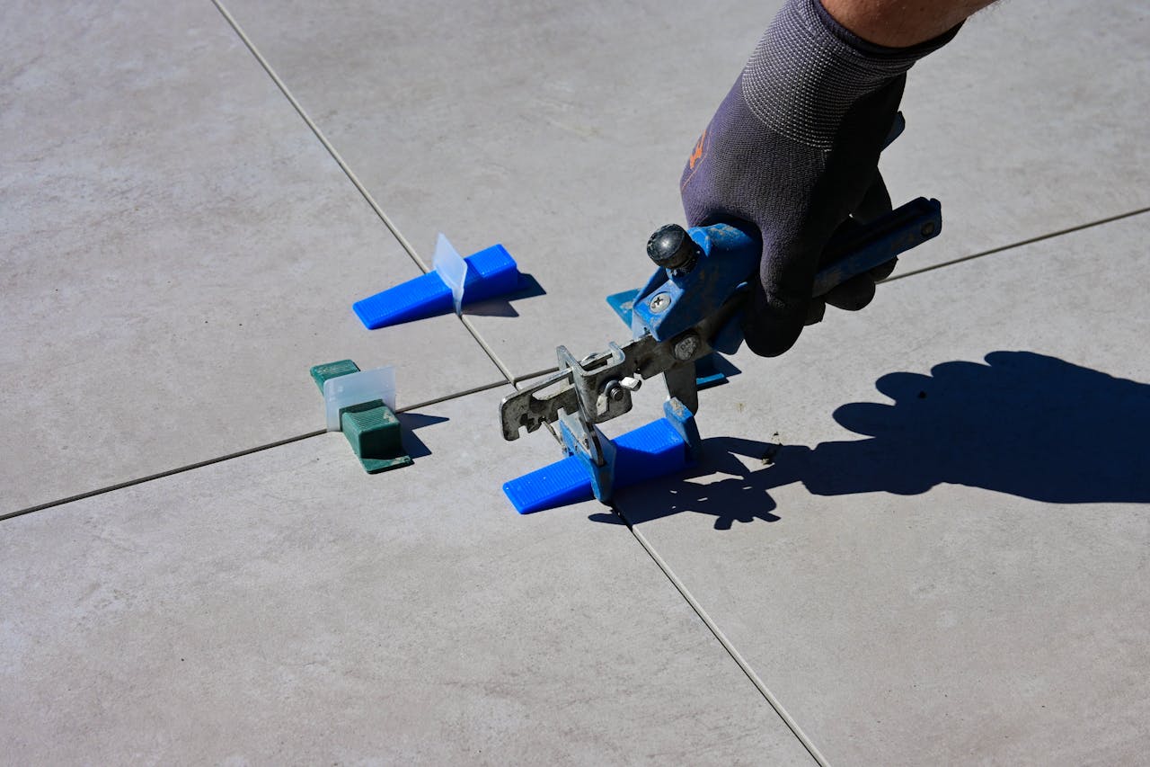 A gloved hand using a leveling tool to install tiles with spacers.